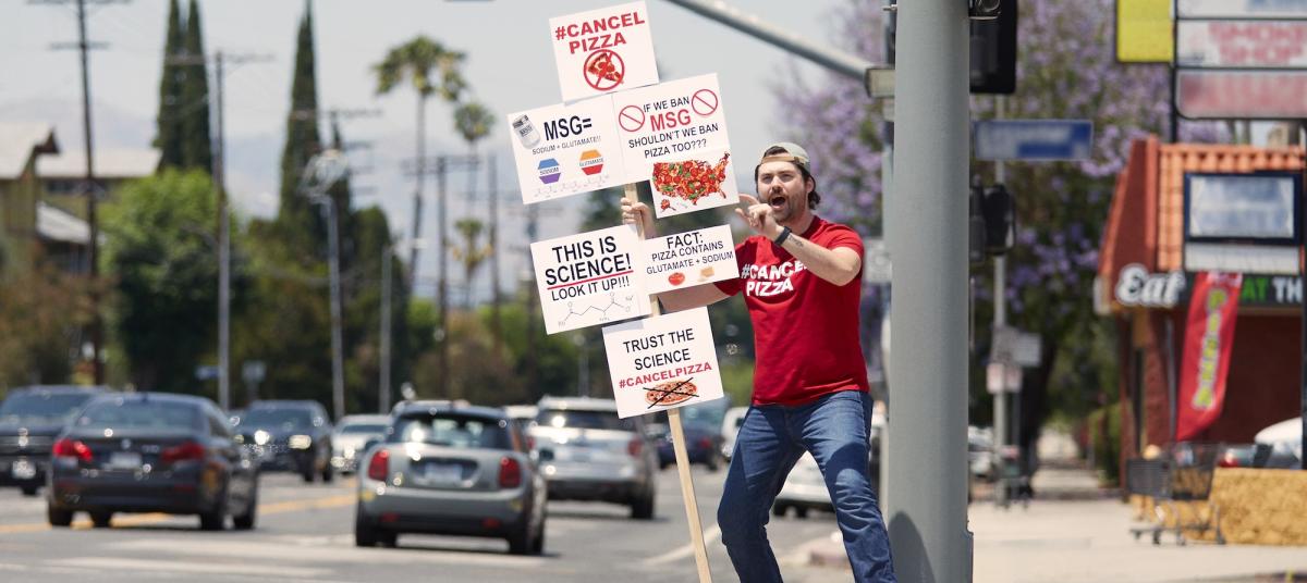man on the street holding #cancelPizza sign